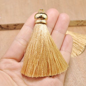 May include: A gold tassel with a gold metal top. The tassel is made of a soft, light brown fabric.