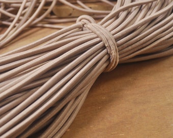 Peut inclure: Gros plan sur un paquet de cordon élastique beige. Le cordon est doux et flexible, idéal pour les projets de bricolage.