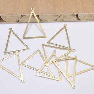 May include: A collection of brass-colored triangle charms. Each charm has a triangular shape with a small loop at the top and a hole at the bottom for attaching to jewelry. The charms are scattered on a white surface.