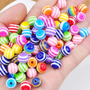 Puede incluir: Una colección de cuentas redondas de colores con rayas. Las cuentas son de plástico y tienen un acabado brillante.