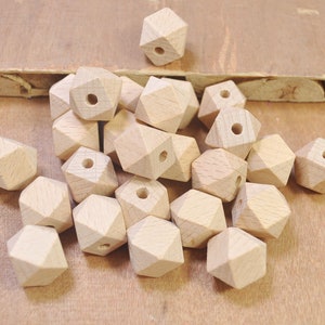 Könnte beinhalten: Eine Sammlung unfertiger geometrischer Holzperlen. Jede Perle hat eine hellbraune Farbe mit mehreren Facetten und einem Loch zum Auffädeln. Die Perlen sind auf einer hellbraunen Oberfläche verstreut.