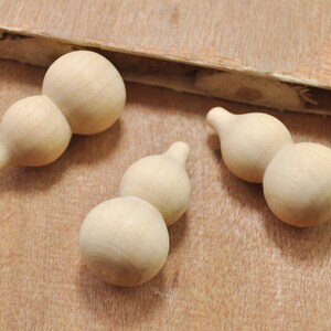 May include: Three wooden gourds, each with two rounded sections, are arranged on a light brown wooden surface. The gourds are unpainted and have a natural wood finish.