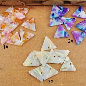 Puede incluir: Tres juegos de cuentas triangulares con forma de concha. El primer juego es rosa y naranja, el segundo juego es morado y azul, y el tercero es blanco y verde. Cada juego está etiquetado con un número.