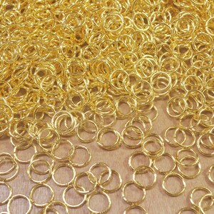 Puede incluir: Un mont&oacute;n grande de anillos de salto dorados, un tipo de anillo de metal utilizado en la fabricaci&oacute;n de joyas.