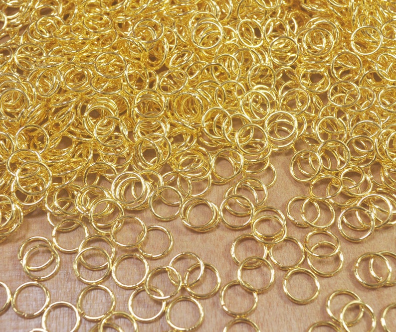 Puede incluir: Un mont&oacute;n grande de anillos de salto dorados, un tipo de anillo de metal utilizado en la fabricaci&oacute;n de joyas.