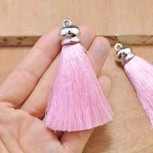 May include: Two pink silk tassels with silver metal caps. The tassels are approximately 2 inches long.