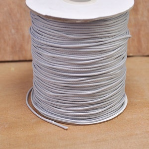 May include: A spool of light gray waxed cord. The cord is wound tightly around a white cardboard spool.