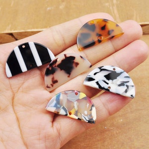 May include: Five half-circle shaped plastic embellishments with different patterns. The patterns include black and white stripes, brown and white marbled, black and white marbled, and multi-colored marbled.
