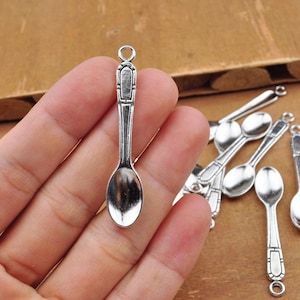 Puede incluir: Encantos de cuchara de plata con un diseño vintage. Las cucharas tienen un cuenco redondeado y un mango decorativo. Los encantos son perfectos para la elaboración de joyas o para agregar un toque único a las manualidades.