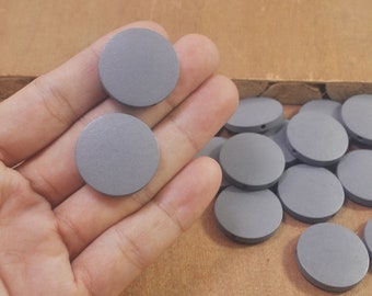 May include: A close-up of a hand holding two gray wooden circles. The circles are smooth and have a slightly textured surface. There are more gray wooden circles in the background.