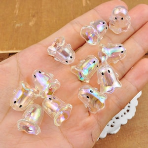 May include: A collection of iridescent clear plastic ghost charms with black eyes. The charms are small and have a translucent, shimmering appearance.