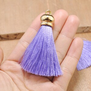 May include: A purple tassel with a gold metal top. The tassel is made of soft, silky threads and is approximately 2 inches long.