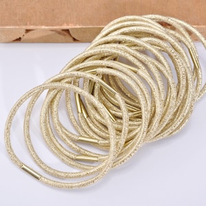 May include: A collection of gold glitter hair ties. Each hair tie is a loop of gold fabric with a metallic gold connector. The hair ties are arranged in a pile, with some overlapping.