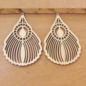 Può includere: Due orecchini in legno non finiti con un design delicato e intricato. Gli orecchini hanno la forma di una lacrima con un motivo circolare al centro e una serie di linee che si irradiano verso l'esterno.