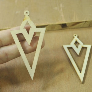 May include: Two unfinished wooden triangle-shaped earrings with a smaller triangle cut out in the center. The earrings have a hole at the top for hanging.