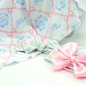 a pink bow and a white blanket with a floral pattern, both resting on a white surface.