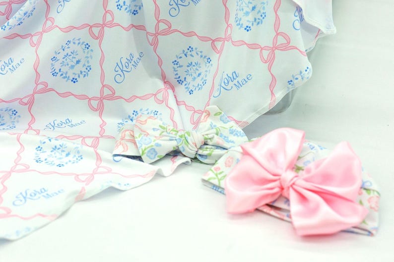 a pink bow and a white blanket with a floral pattern, both resting on a white surface.