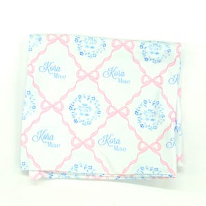 a white fabric with a pink floral pattern and the name 'Kora Mae' written in blue.