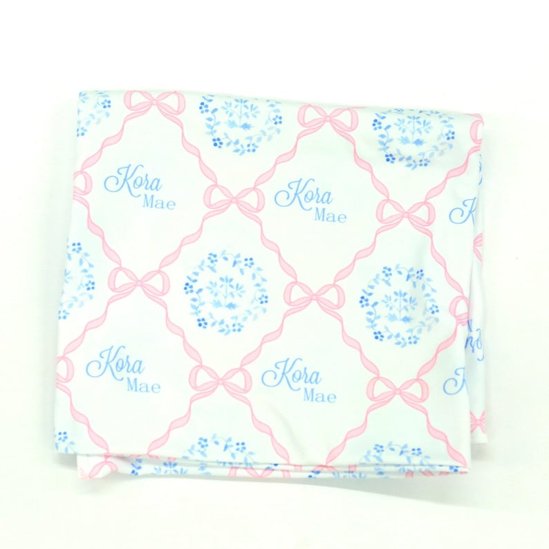 a white fabric with a pink floral pattern and the name 'Kora Mae' written in blue.