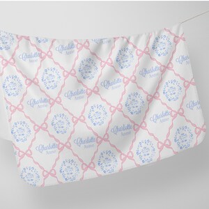 a white fabric with a repeating pattern of pink bows and the name "Charlotte" written in blue.