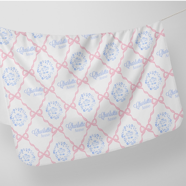 a white fabric with a repeating pattern of pink bows and the name "Charlotte" written in blue.
