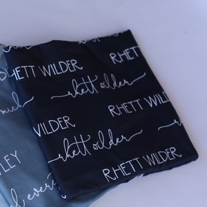 May include: Two fabric squares with the name "Rhett Wilder" printed in white on a black background and a blue background.