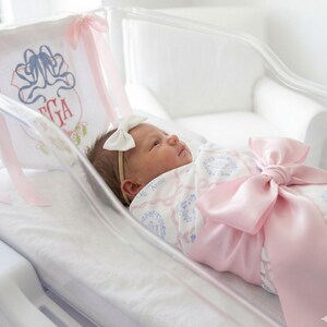 A newborn baby girl is peacefully sleeping in a hospital bed, wearing a pink bow and a white blanket with a floral pattern.