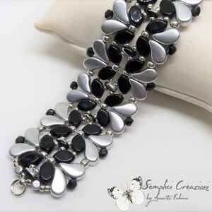 May include: A beaded bracelet featuring a repeating pattern of silver and black petal-shaped beads, accented with small metallic silver spheres and tiny black faceted beads. The bracelet includes a silver-toned metal ring clasp at one end.
