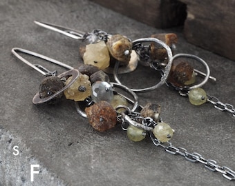 May include: A pair of silver earrings with a cluster of amber and clear quartz stones, connected by a silver chain. The earrings are dangling and have a rustic, organic feel.