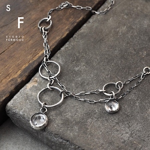 Puede incluir: Un collar de plata con múltiples eslabones de cadena y colgantes circulares. El collar tiene un acabado texturizado y presenta dos pequeñas piedras redondas y transparentes.