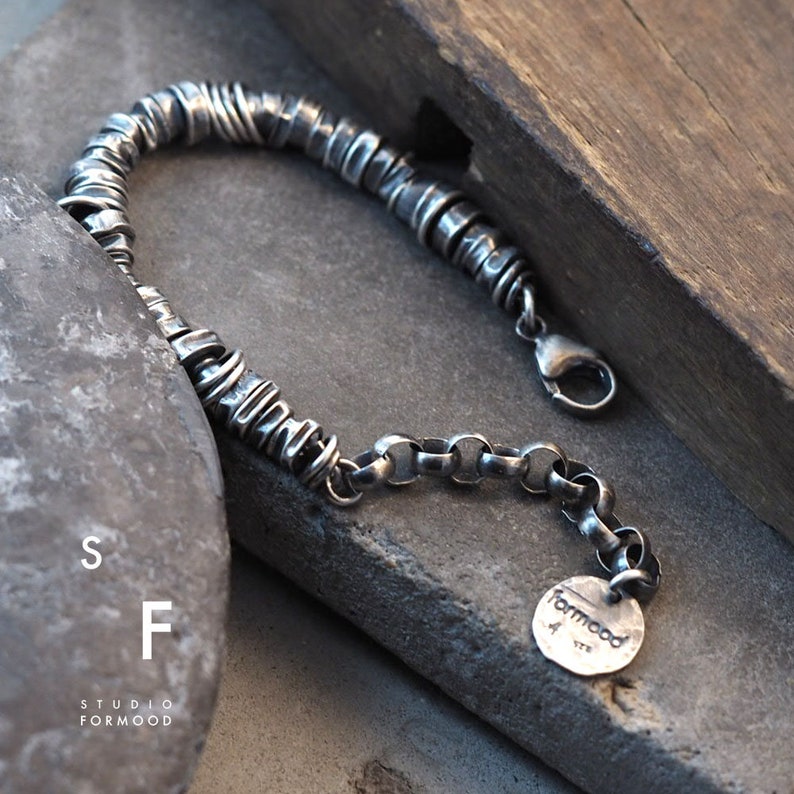 May include: A silver bracelet with a chain and a circular charm that says "formood".