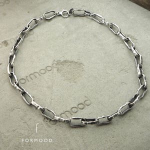 Puede incluir: Un collar de cadena plateada con un dise&ntilde;o de eslabones irregulares y texturizados. El collar se muestra sobre una superficie gris. La palabra "formood" y el nombre de la marca "FORMOOD" son visibles.