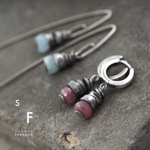Può includere: Un paio di orecchini d'argento con pietre preziose rosa e blu. Gli orecchini sono realizzati con un design a filo ritorto e hanno una chiusura ad anello.