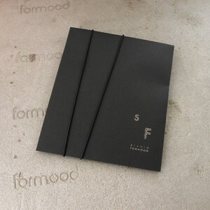 May include: Black envelope with two black elastic bands and the text "S F Studio Formood" printed in white.