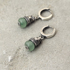 May include: A pair of silver hoop earrings with a green stone pendant. The stone is set in a textured silver setting.