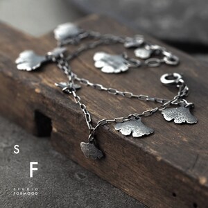 May include: A silver chain bracelet with multiple ginkgo leaf charms. The bracelet is on a wooden surface.