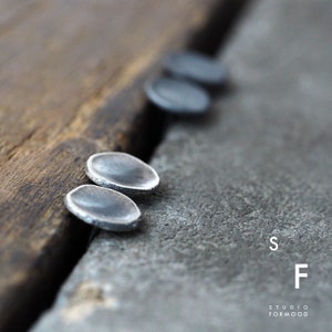 Peut inclure: Quatre boucles d'oreilles rondes, légèrement concaves, de couleur argentée, posées sur une surface en bois. Les boucles d'oreilles sont disposées en ligne, les deux les plus proches du spectateur étant nettes.