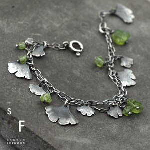 Peut inclure: Un bracelet en argent avec une double rang&eacute;e de maillons. Le bracelet est orn&eacute; de plusieurs breloques en forme de feuilles de ginkgo avec des pierres pr&eacute;cieuses vertes attach&eacute;es. Le bracelet se ferme avec un fermoir &agrave; mousqueton.