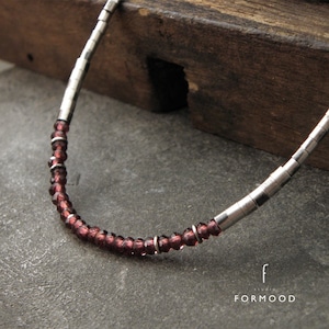 May include: A silver chain necklace with small, dark red beads. The necklace is on a wooden surface.