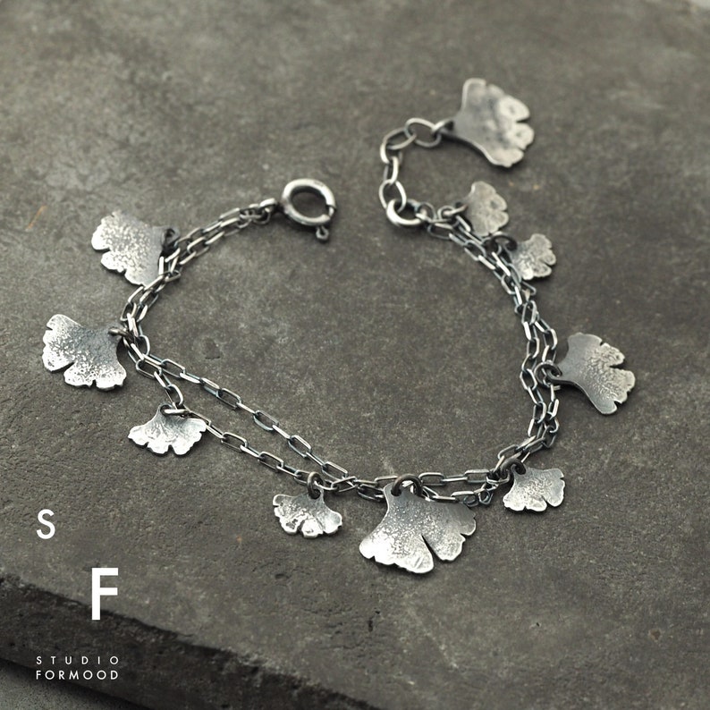 May include: A silver bracelet with a delicate chain and multiple ginkgo leaf charms. The leaves have a textured surface and are connected to the chain with small loops.