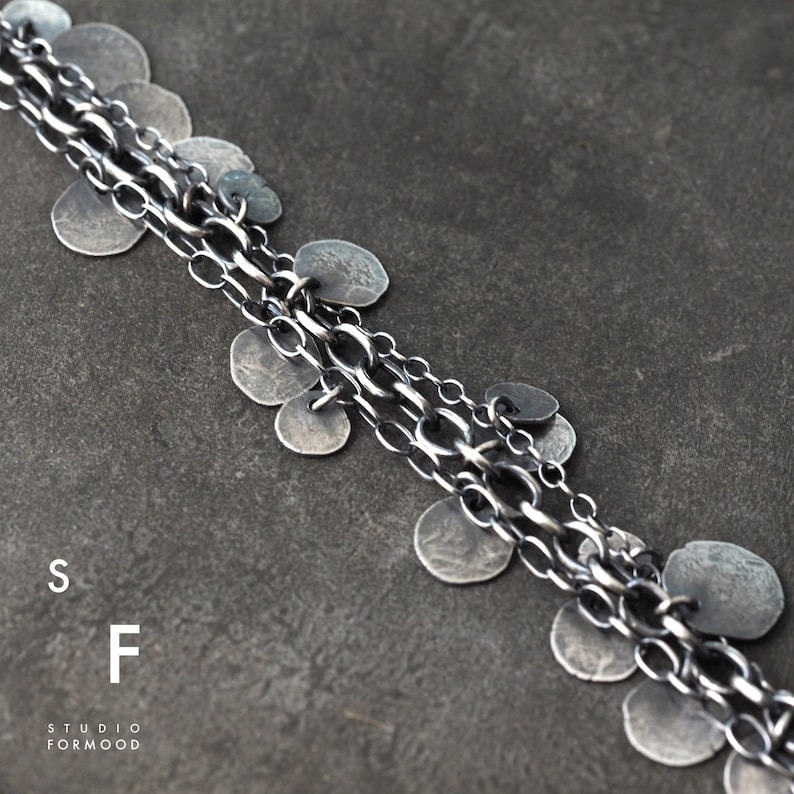 May include: A silver chain necklace with multiple strands and small, round silver charms. The necklace is on a gray background.