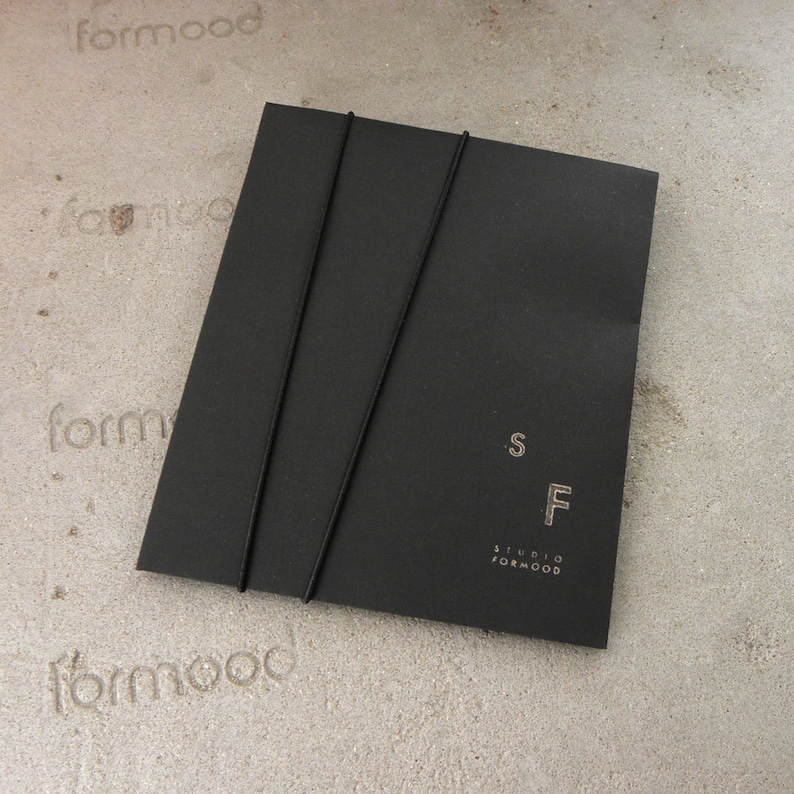 May include: Black envelope with two black elastic bands and the text "Studio Formwood" and "SF" in white.