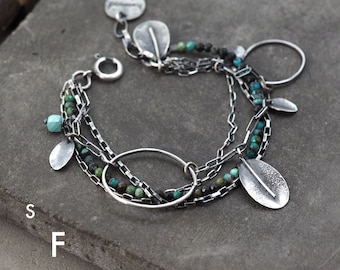 May include: A silver bracelet with multiple chains, turquoise and black beads, and silver leaf charms. The bracelet has a circle charm and a small oval charm.