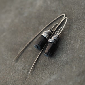 Pode incluir: Um par de brincos de prata com detalhes em pedra preta. Os brincos são longos e pendentes, com um design simples de fio.