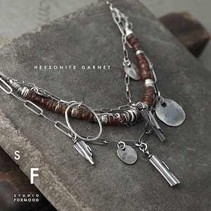 Può includere: Una collana a catena d'argento a più strati con perline di granato hessonite marrone e ciondoli d'argento. La collana presenta un ciondolo circolare, due ciondoli rettangolari e tre ciondoli rotondi. Il testo "Hessonite Garnet" è visibile nell'immagine.