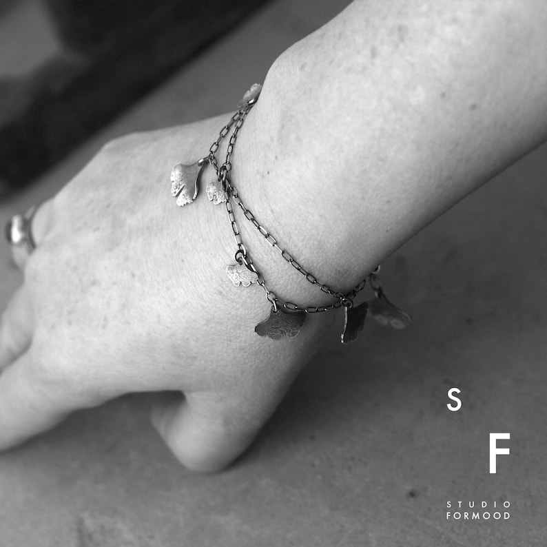 May include: A silver bracelet with multiple ginkgo leaf charms. The bracelet is on a person's wrist. The text "S F STUDIO FORMOOD" is visible in the lower right corner of the image.