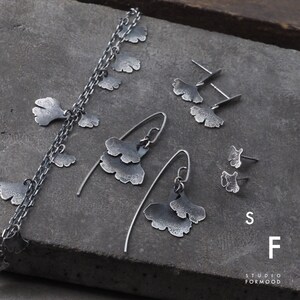 May include: A set of silver jewelry featuring ginkgo leaf designs. The set includes a necklace, a pair of long drop earrings, and a pair of stud earrings. The jewelry is made by Studio Formmood.