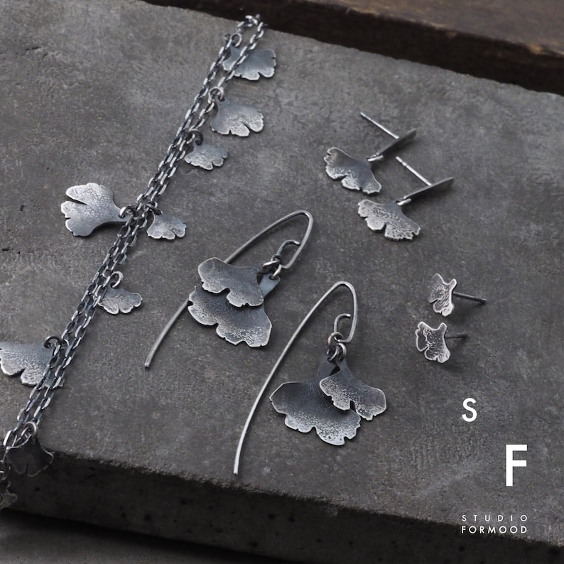 May include: A set of silver jewelry featuring ginkgo leaf designs. The set includes a necklace, a pair of long drop earrings, and a pair of stud earrings. The jewelry is made by Studio Formmood.