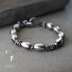 May include: A silver bracelet with oval-shaped beads and a clasp. The bracelet is made of metal and has a polished finish.