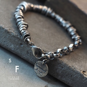 May include: Silver bracelet featuring a chain and a series of stacked rings. The bracelet has a clasp and a small silver tag with the word "formmood" on it.